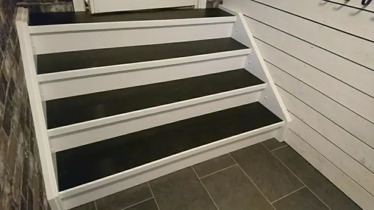 Utvändig entrétrappa med svarta steg mot vit fasadpanel